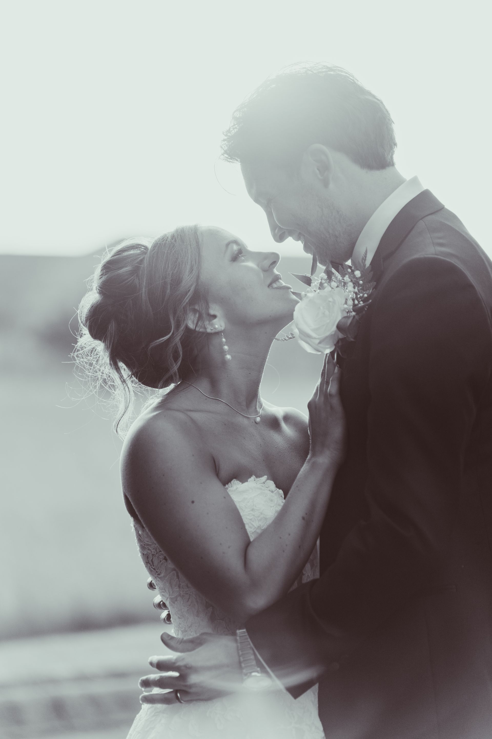 Bride and groom embracing, looking at each other lovingly, lit by bright sunlight. Black and white photo.