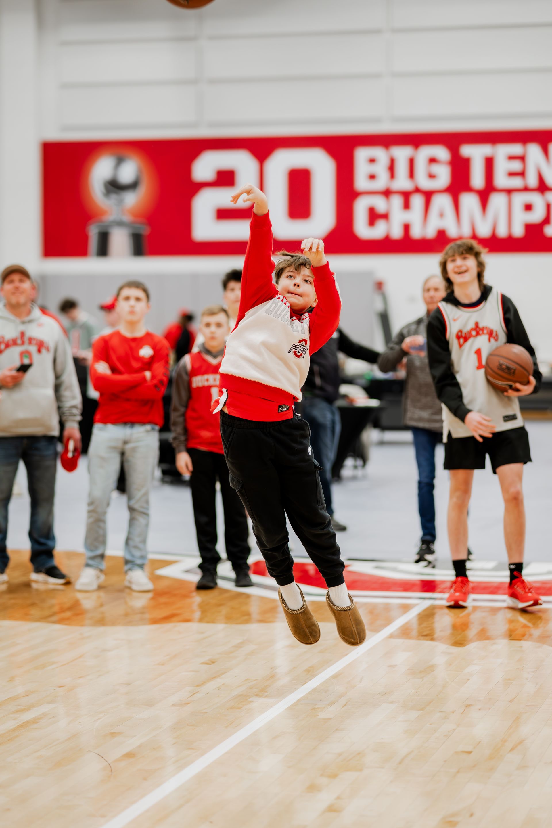 Young person jumping, shooting basketball in a gym; Ohio State banner in background.Midwest Cards | Event Photography