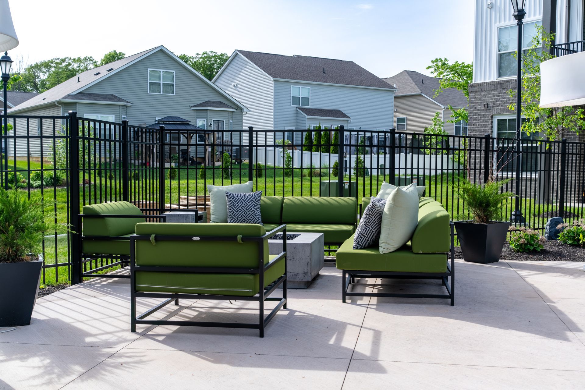 A patio with green furniture and a black fence in front of a house.