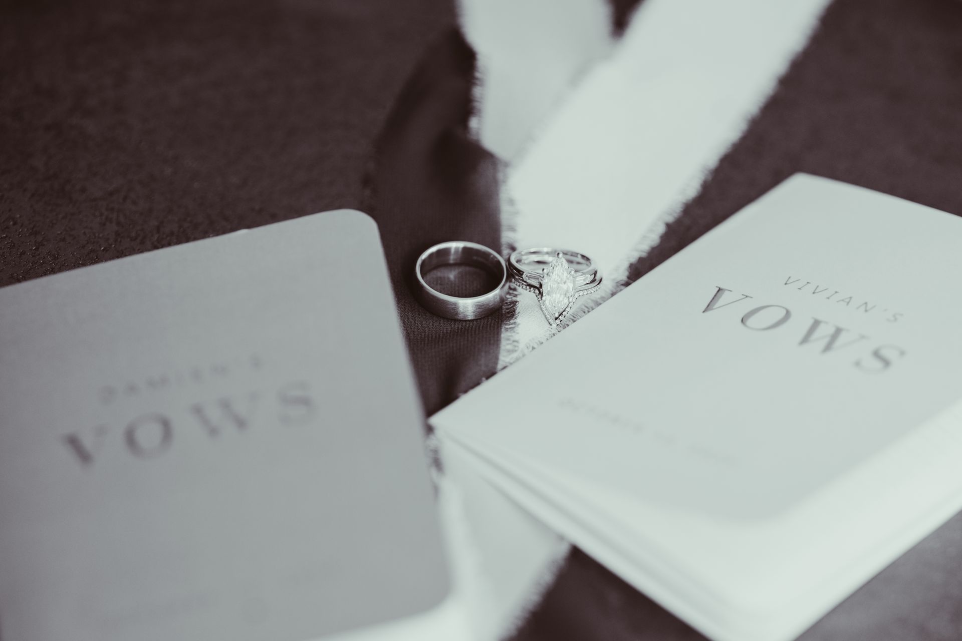 Two vow books and wedding rings on dark fabric, with white ribbon.