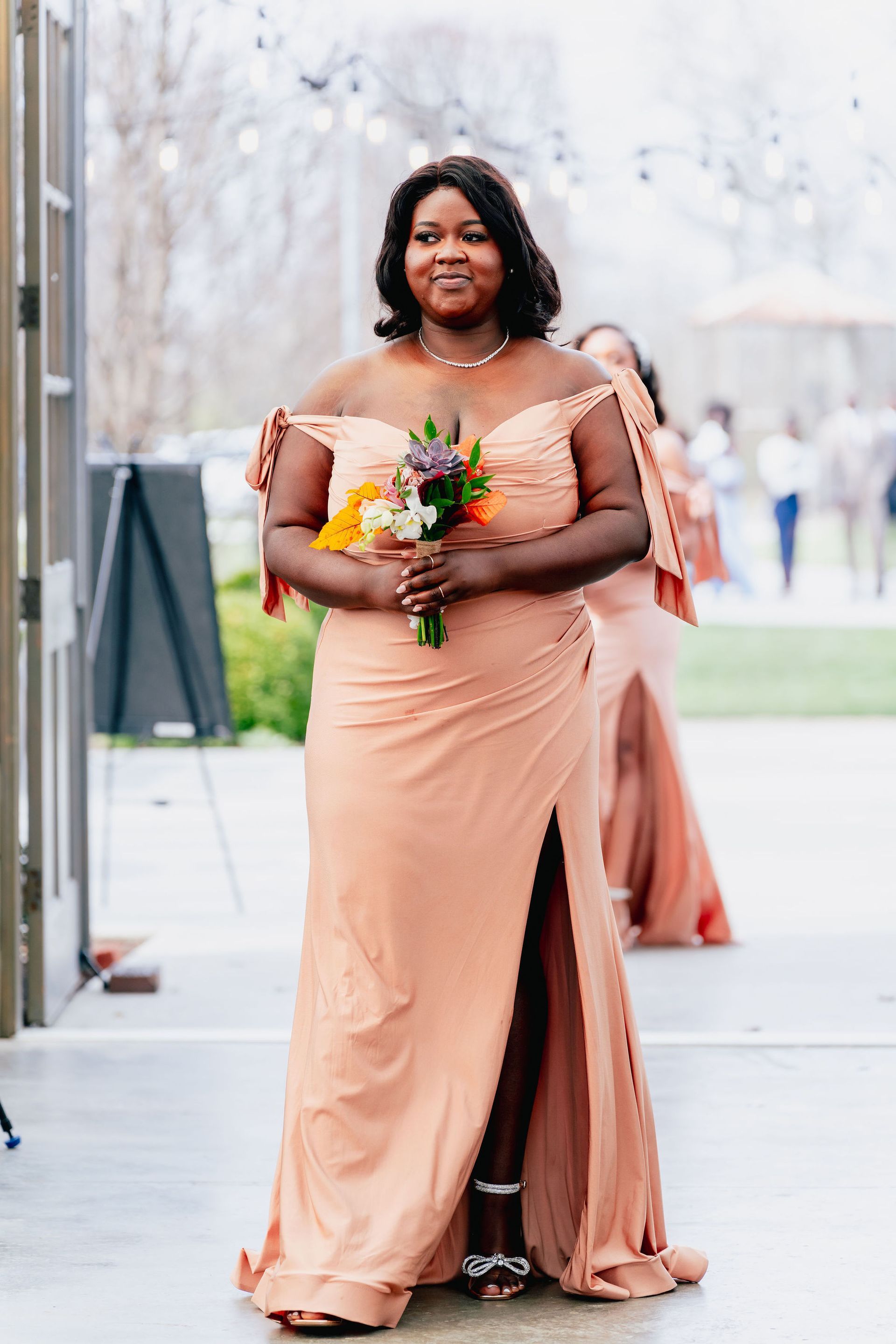 A woman in a peach bridesmaid dress is holding a bouquet of flowers.