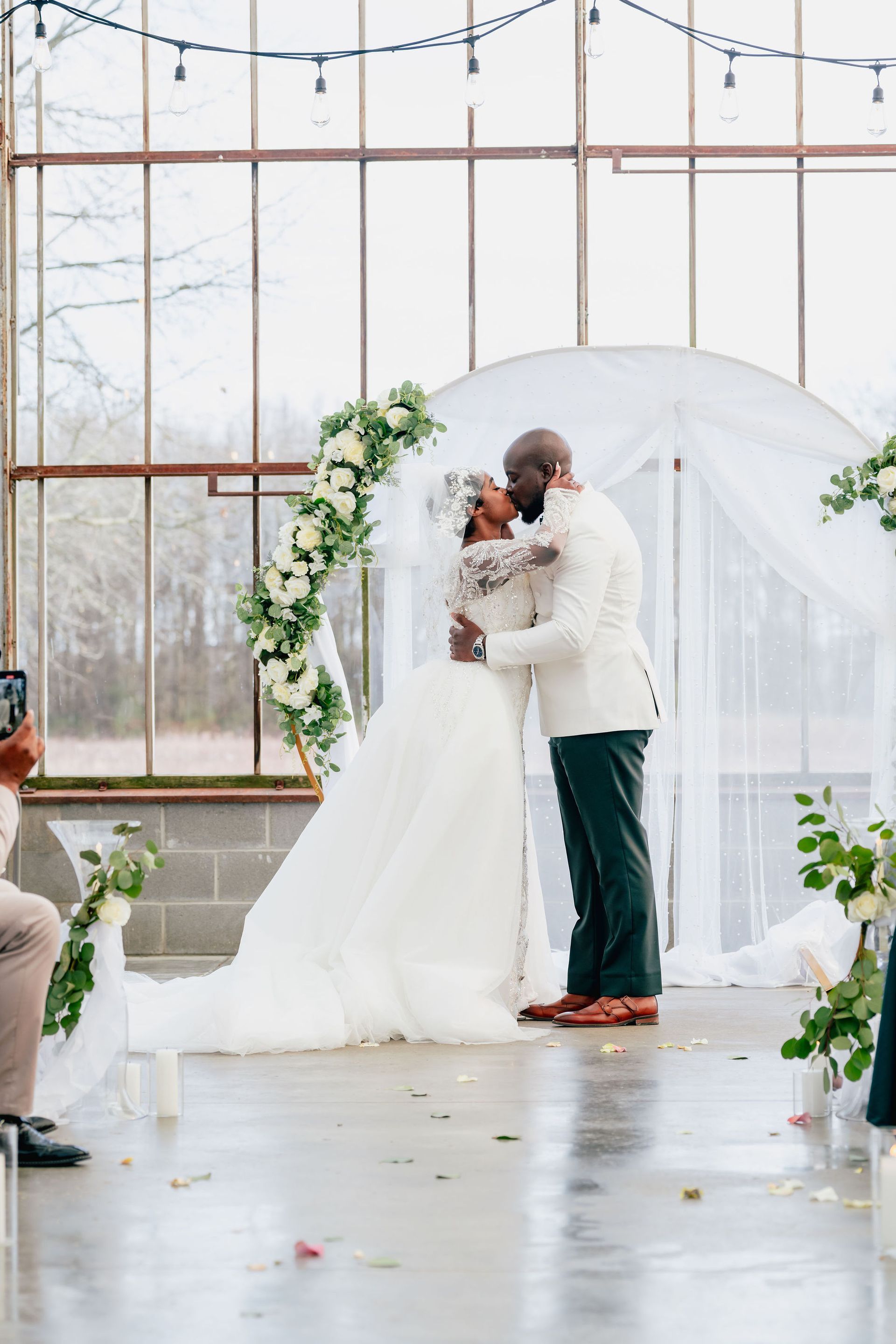A bride and groom kissing during their wedding ceremony in front of a large window.