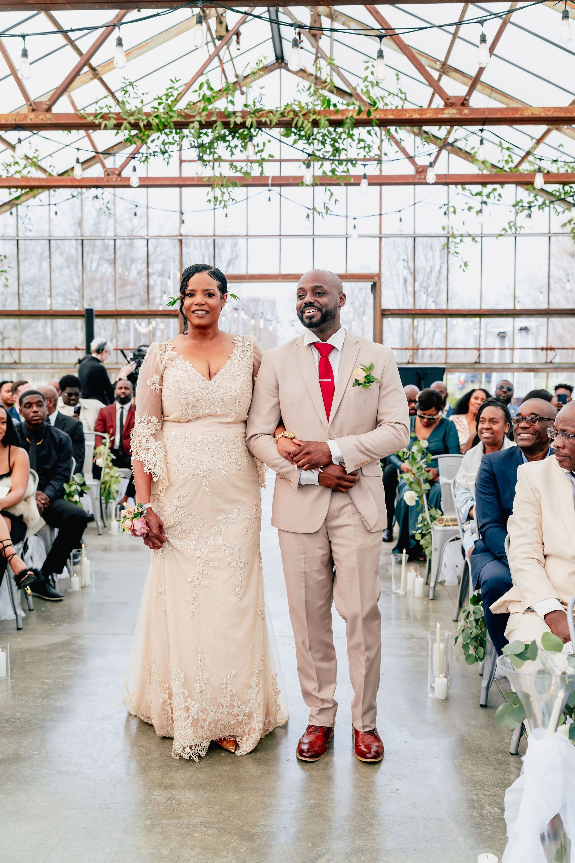 A bride and groom are walking down the aisle at their wedding in a greenhouse.