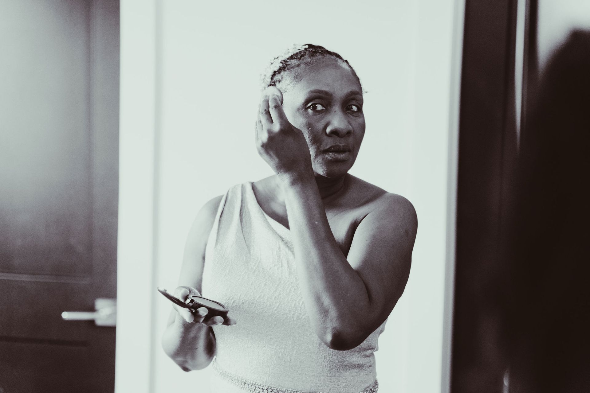 A black and white photo of a woman looking at herself in a mirror.