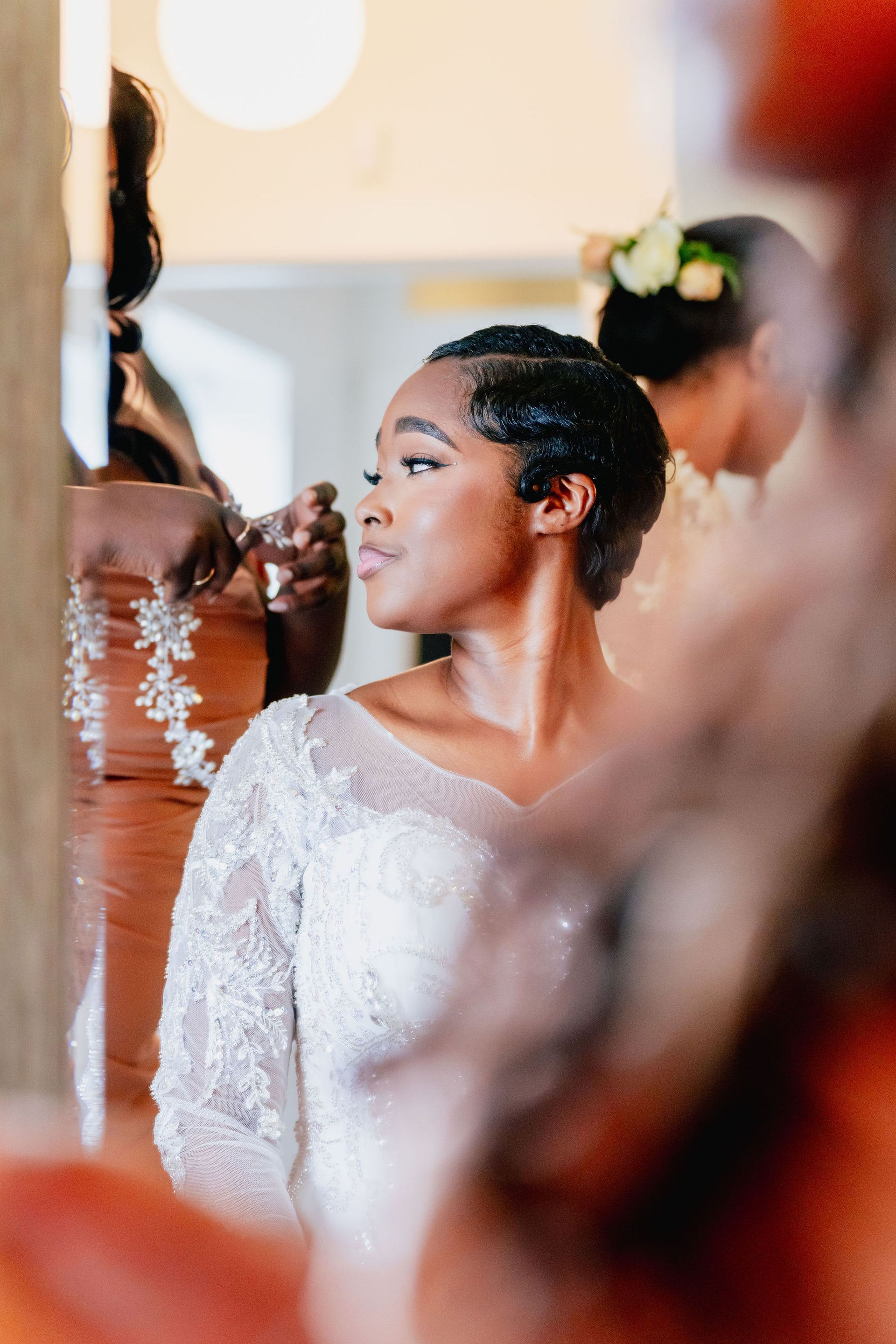 A woman in a wedding dress is getting her hair done in front of a mirror.