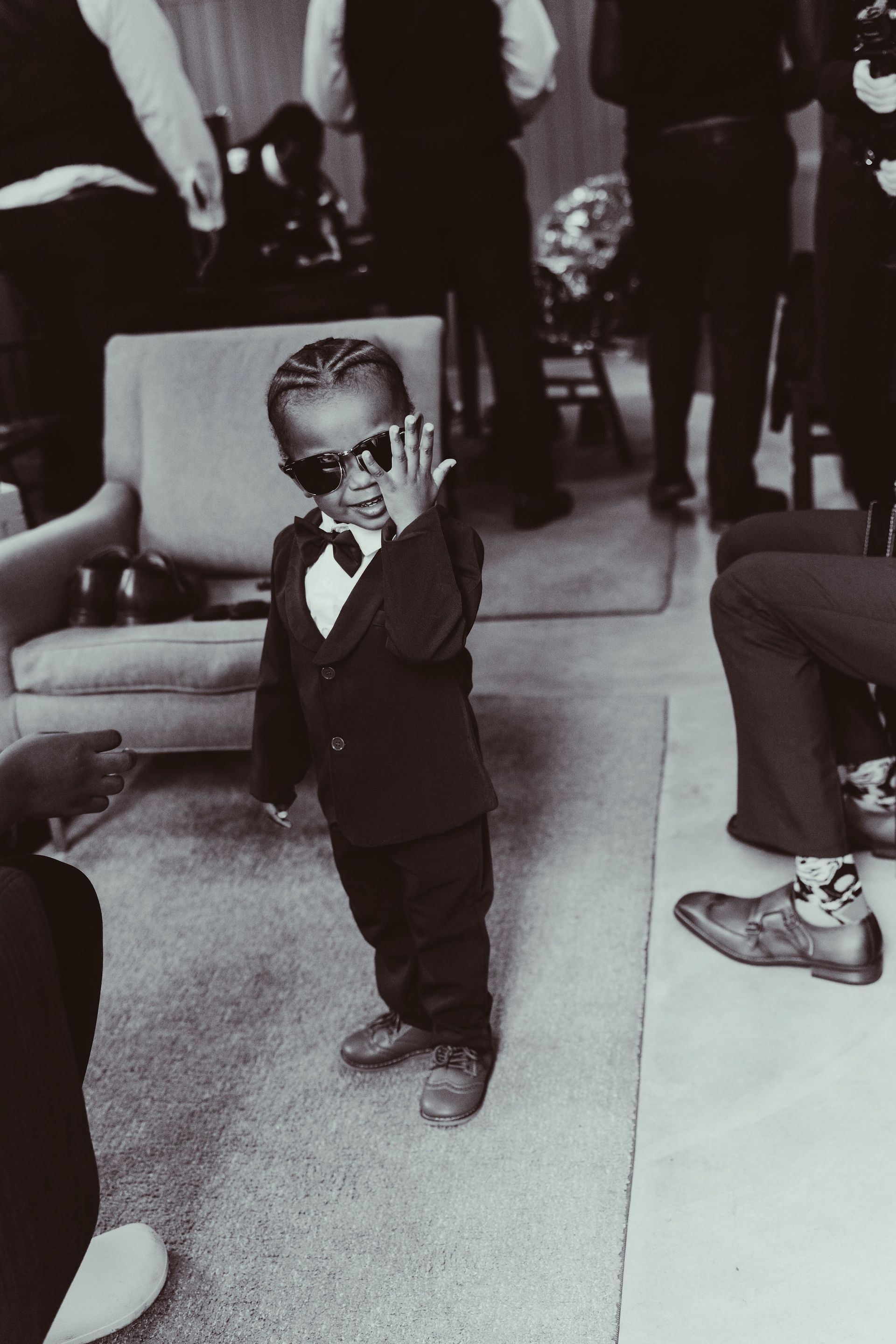 A little boy wearing sunglasses and a tuxedo