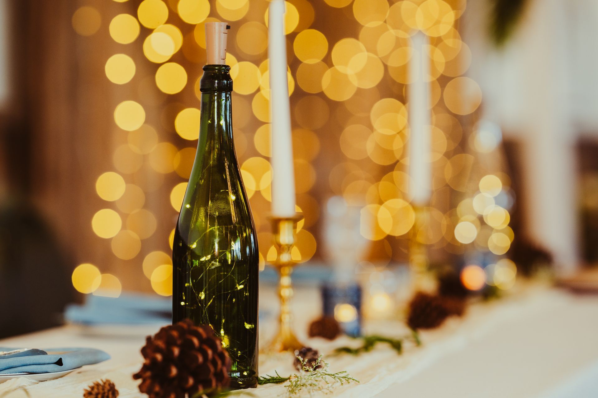 A bottle of wine is sitting on a table with candles and pine cones.