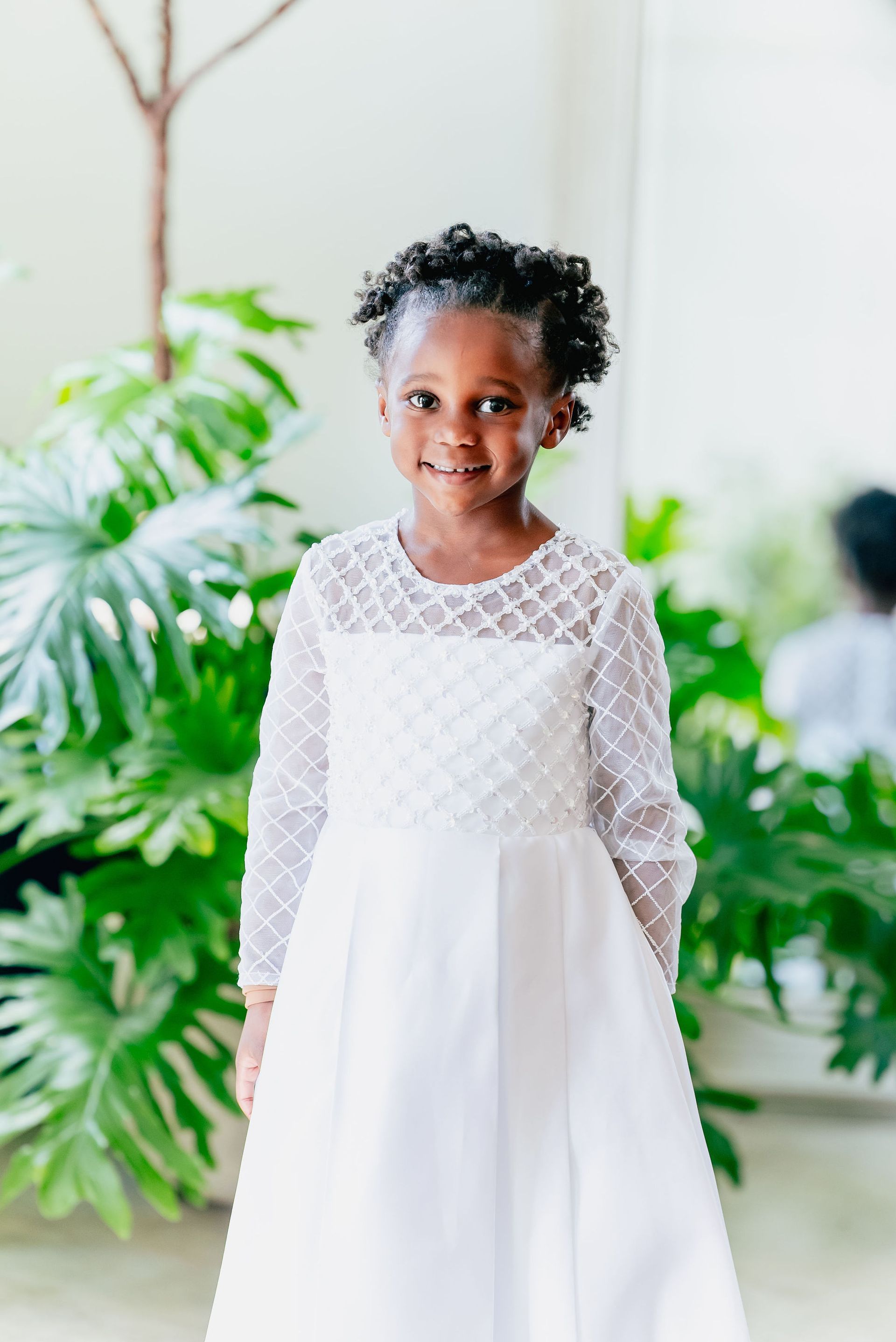 A little girl in a white dress is standing in front of a mirror.
