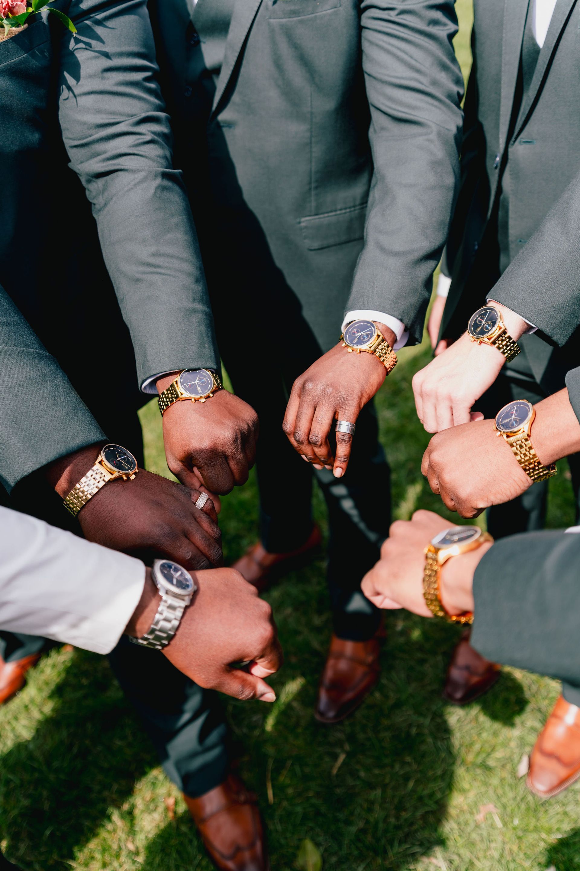 A group of men wearing suits and watches are putting their hands together.
