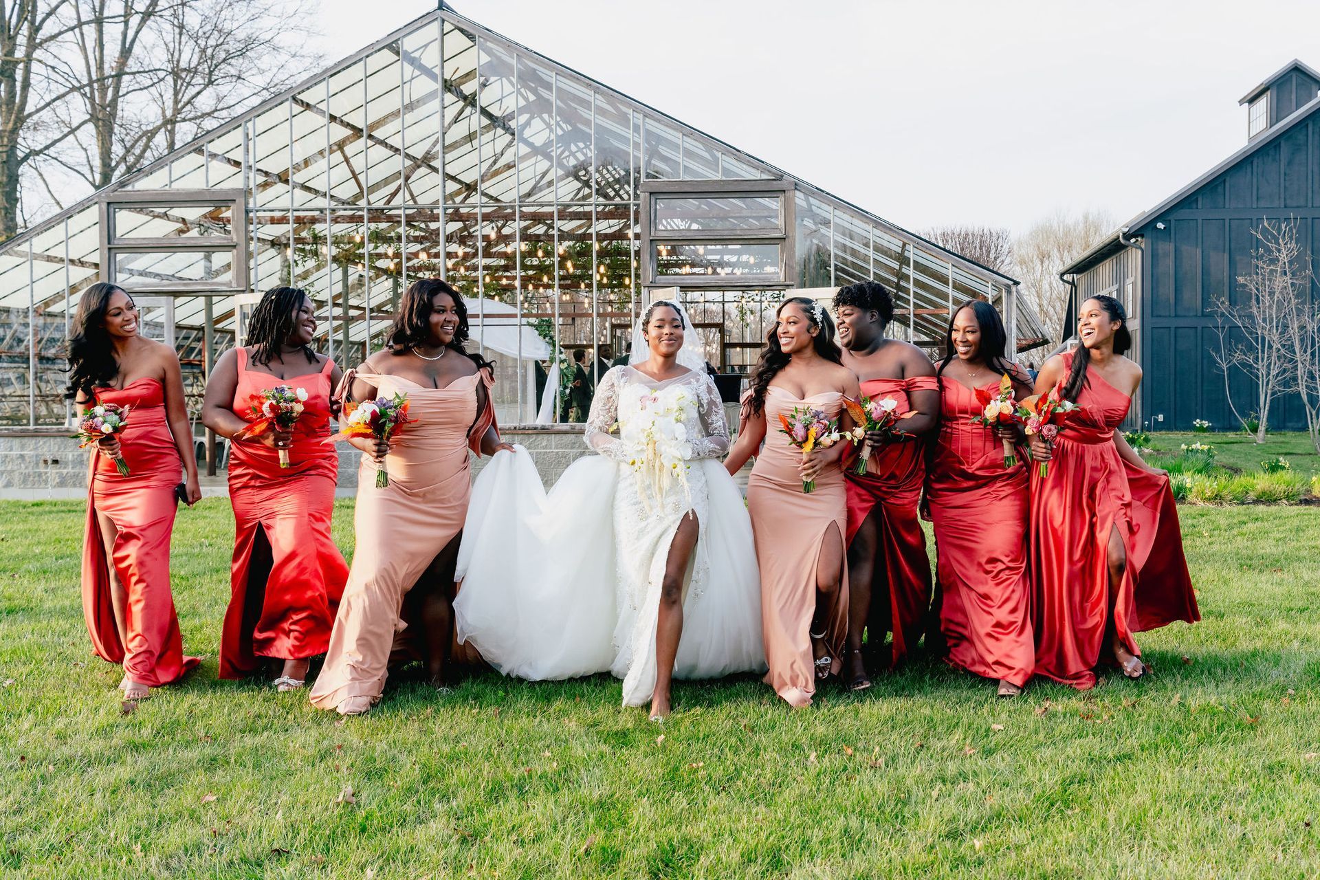 A bride and her bridesmaids are posing for a picture in front of a greenhouse.
