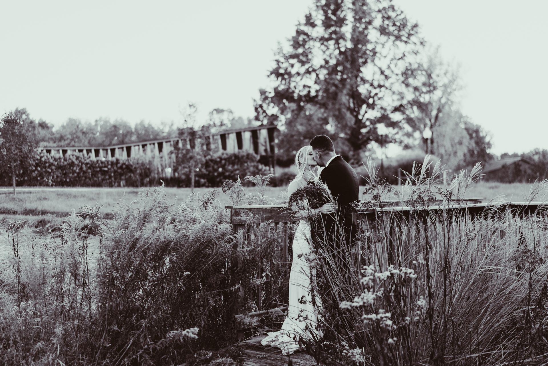 A bride and groom are kissing on a bridge over a body of water.