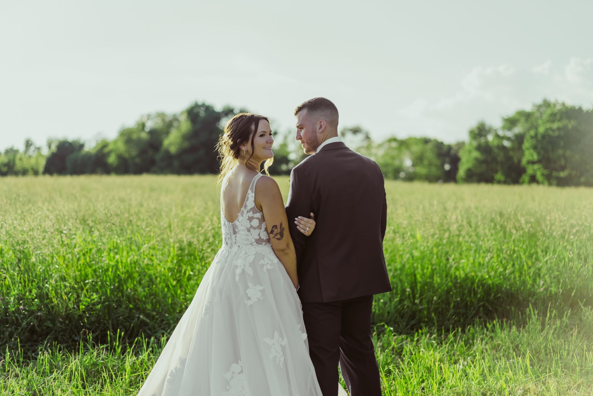 A bride and groom are standing in a field holding hands.