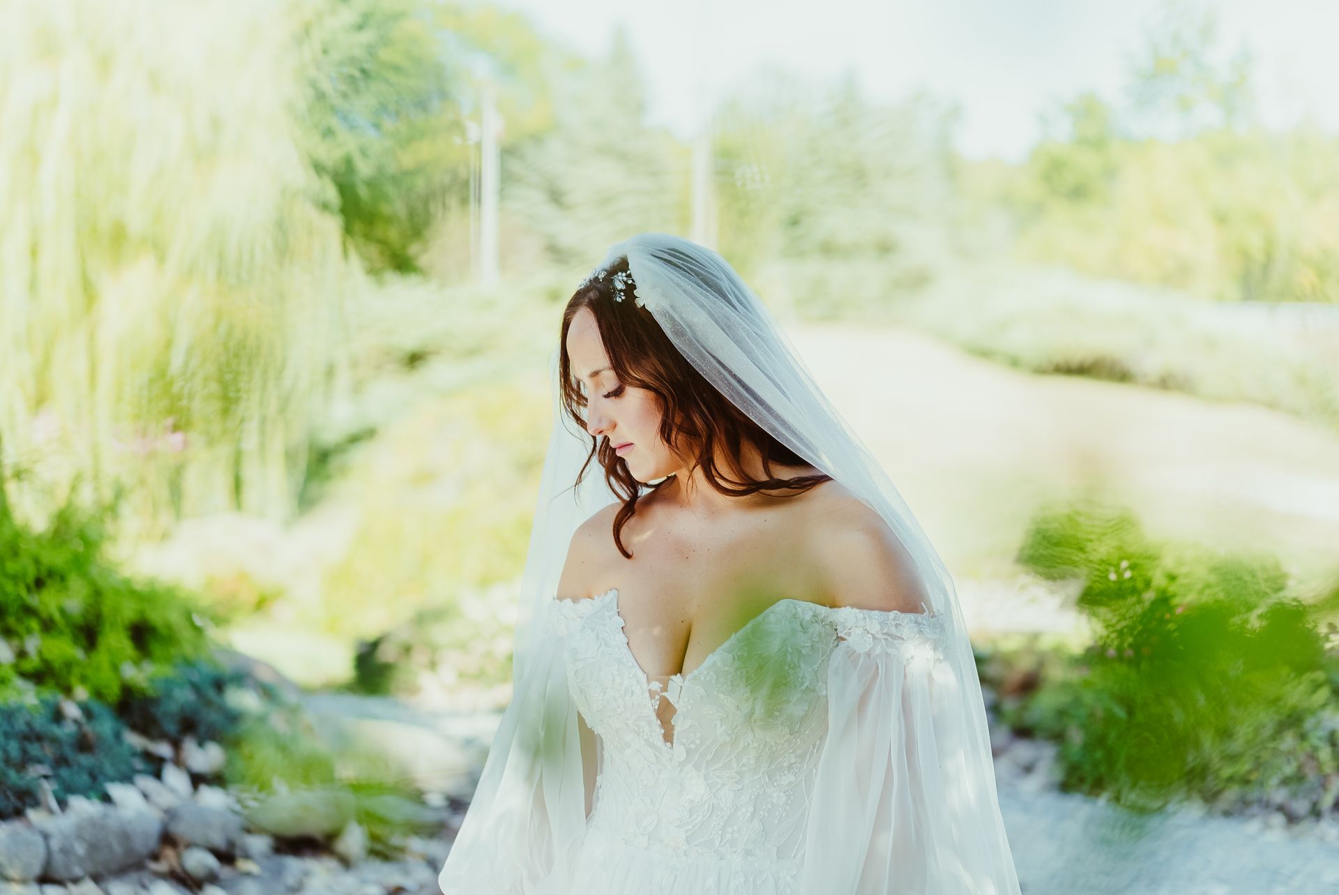 A bride in a wedding dress and veil is standing next to a river.