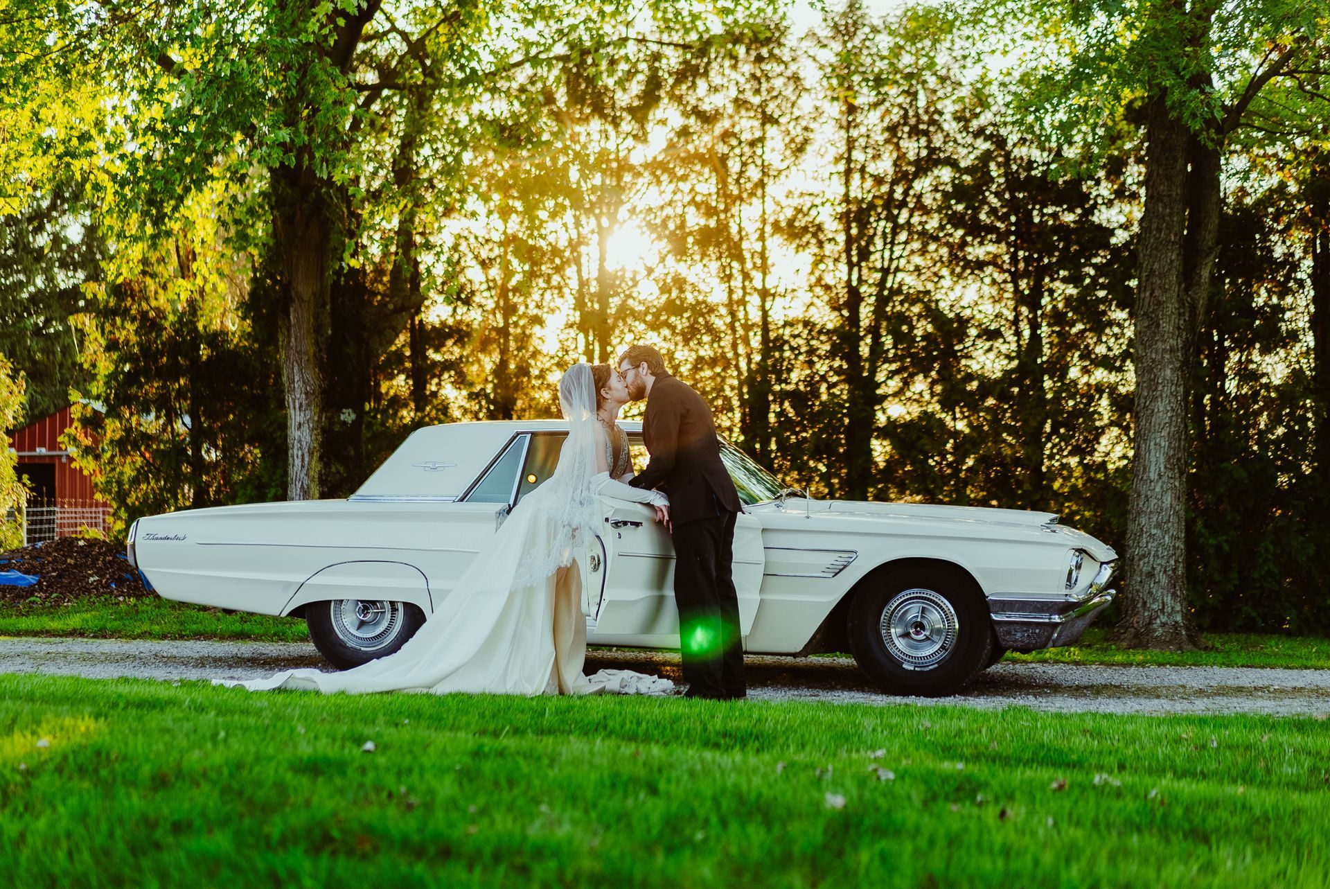 A bride and groom kissing in front of a white car.