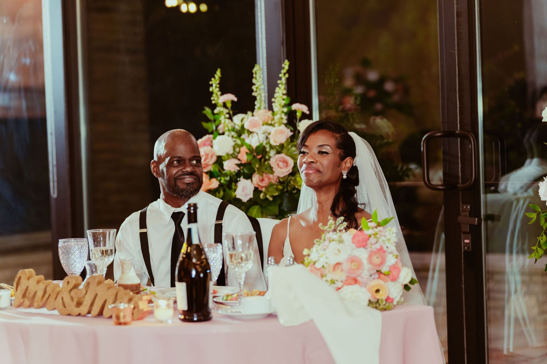 A bride and groom are sitting at a table at their wedding reception.