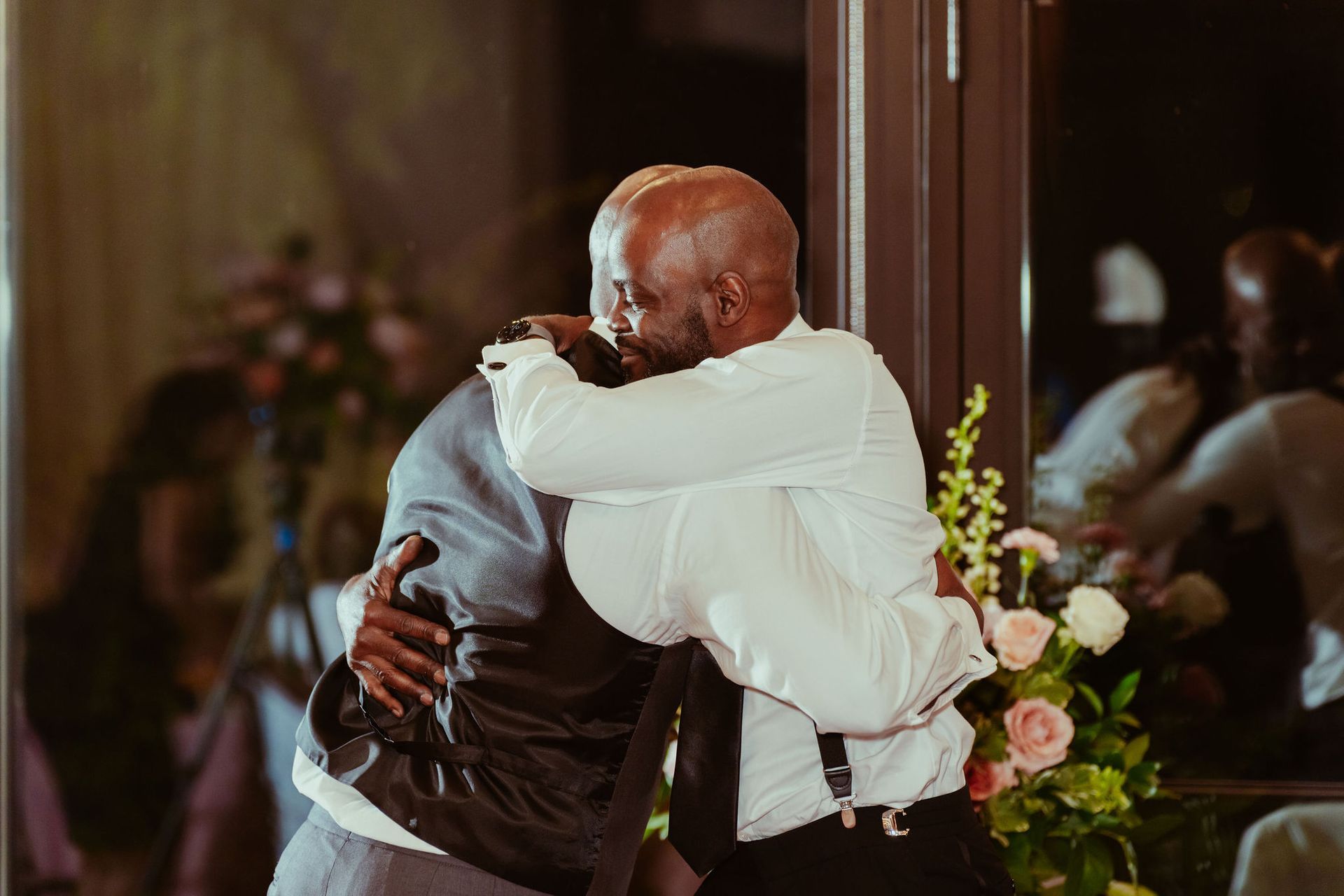 Two men are hugging each other at a wedding reception.