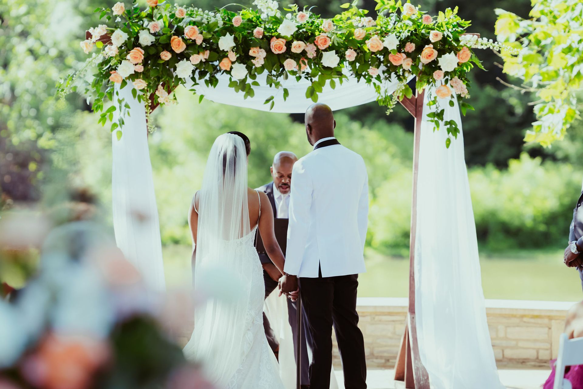 A bride and groom are holding hands during their wedding ceremony under an arch decorated with flowers.