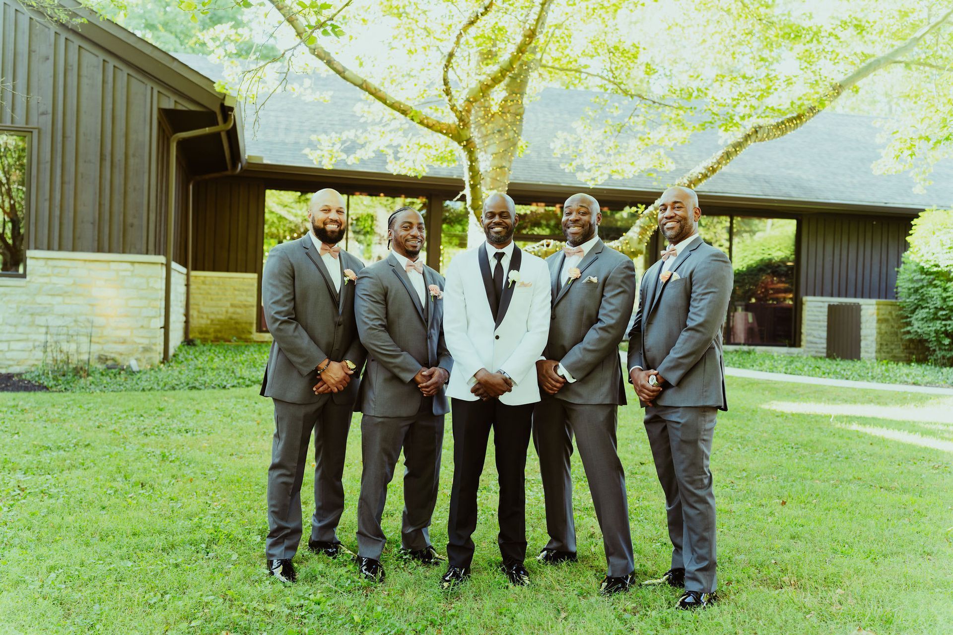 The groom and his groomsmen are posing for a picture in front of a house.