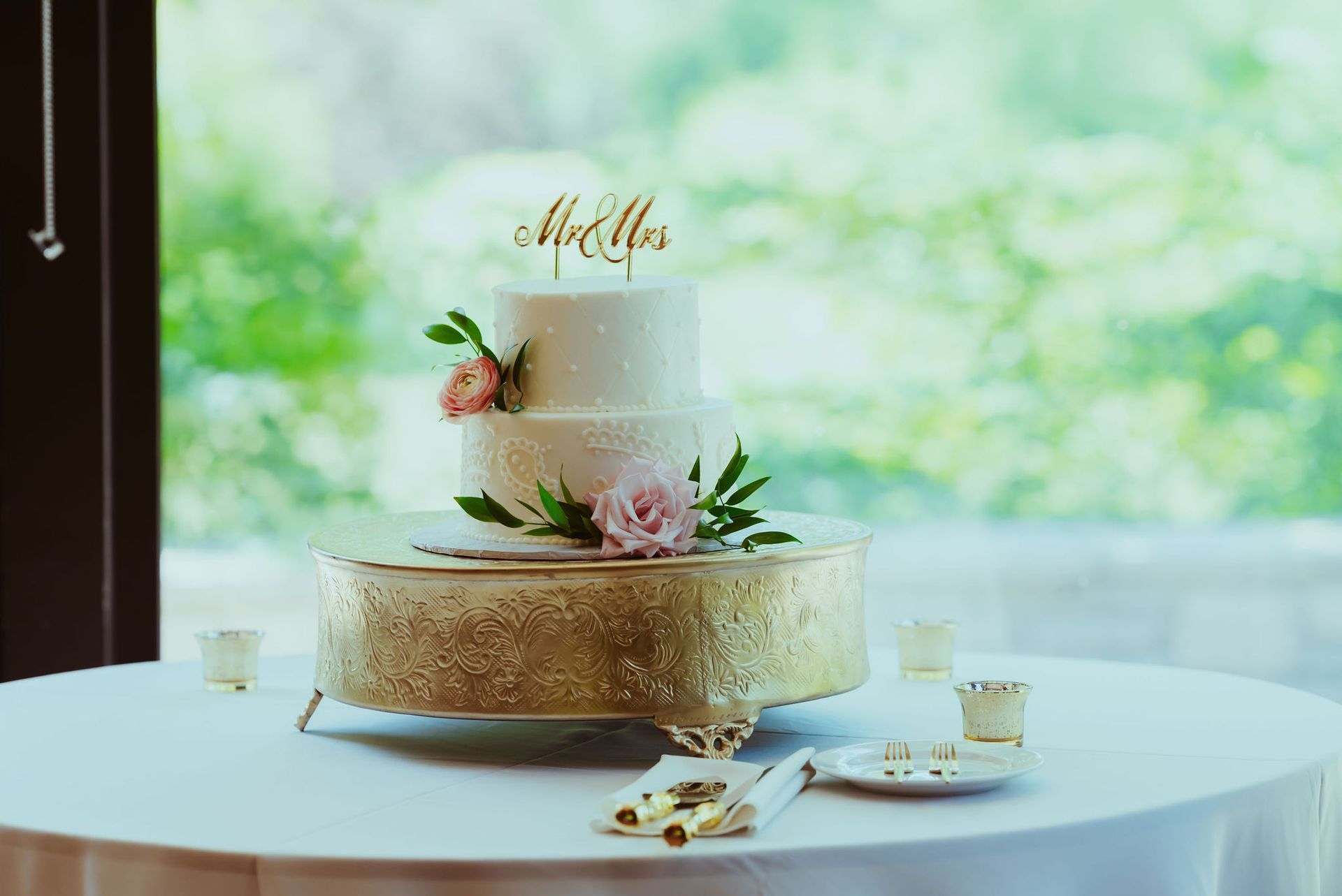 A wedding cake is sitting on top of a gold cake stand on a table.