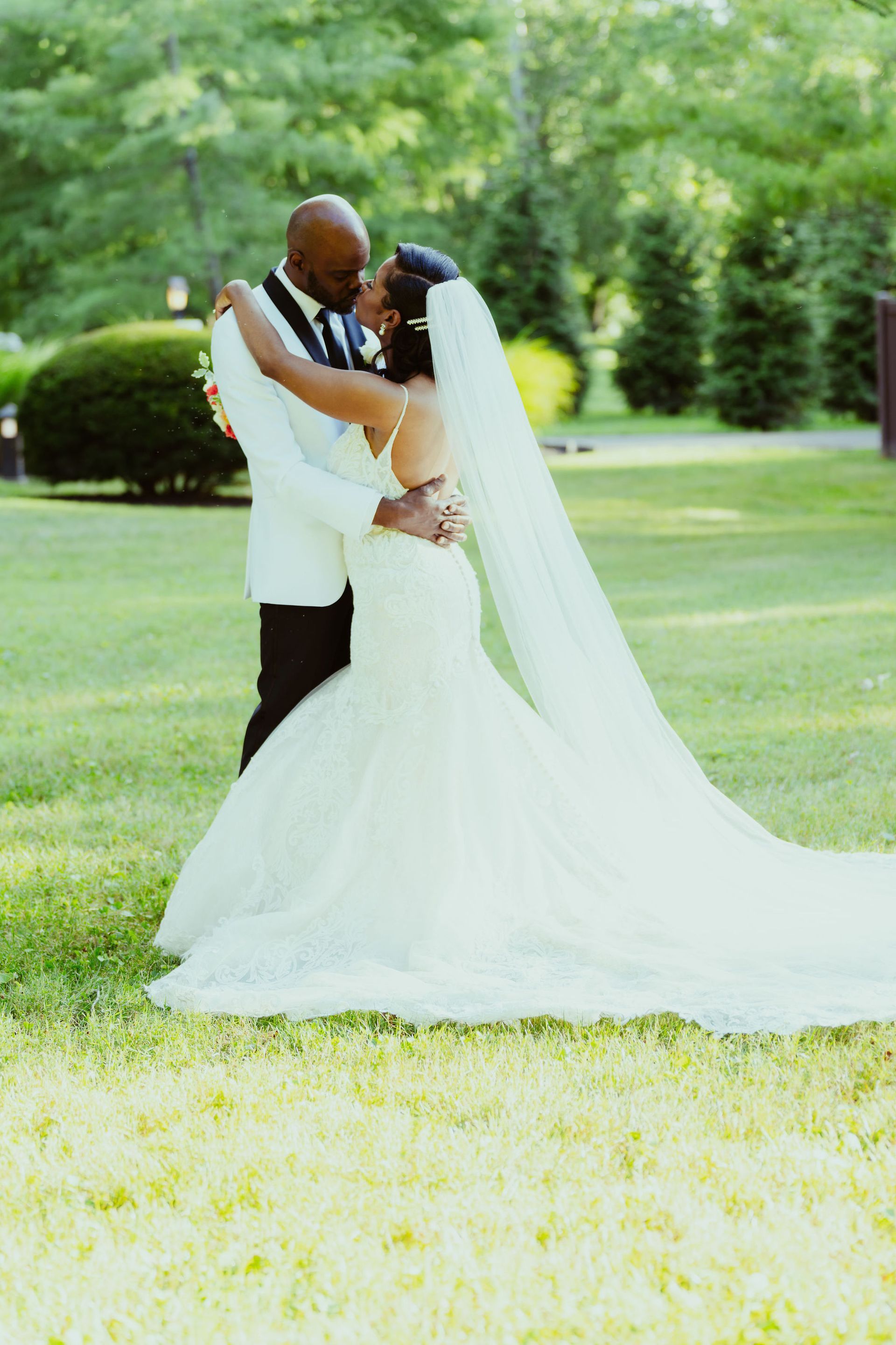 A bride and groom are kissing in the grass.