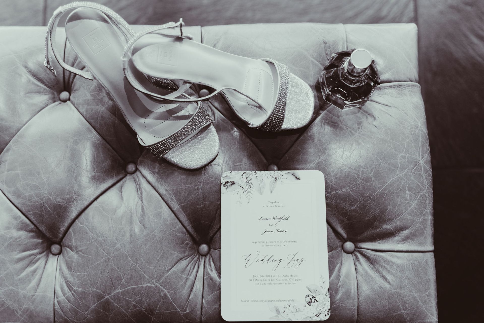 A pair of shoes and a wedding invitation are on a leather ottoman.