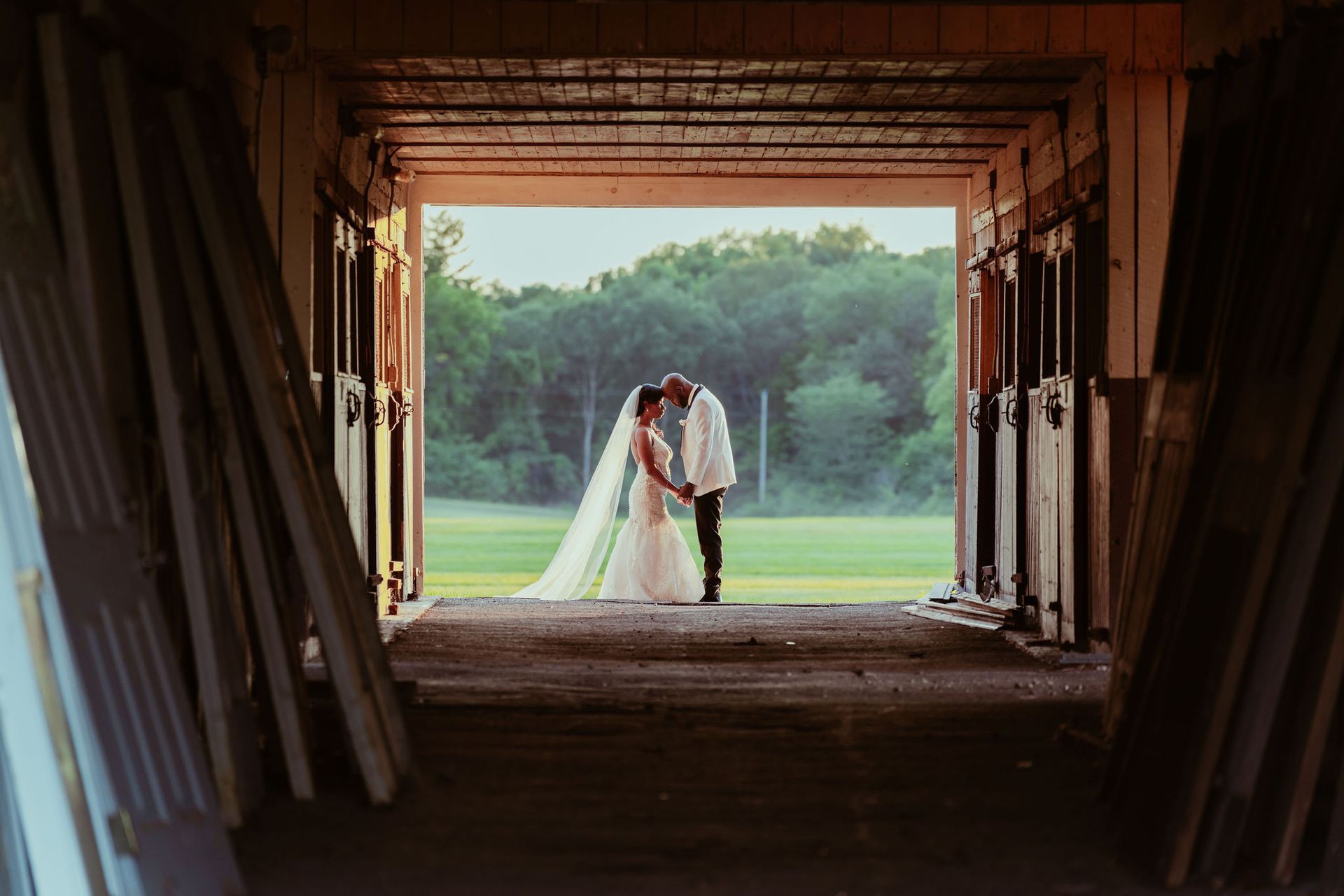 A bride and groom are kissing in a barn.