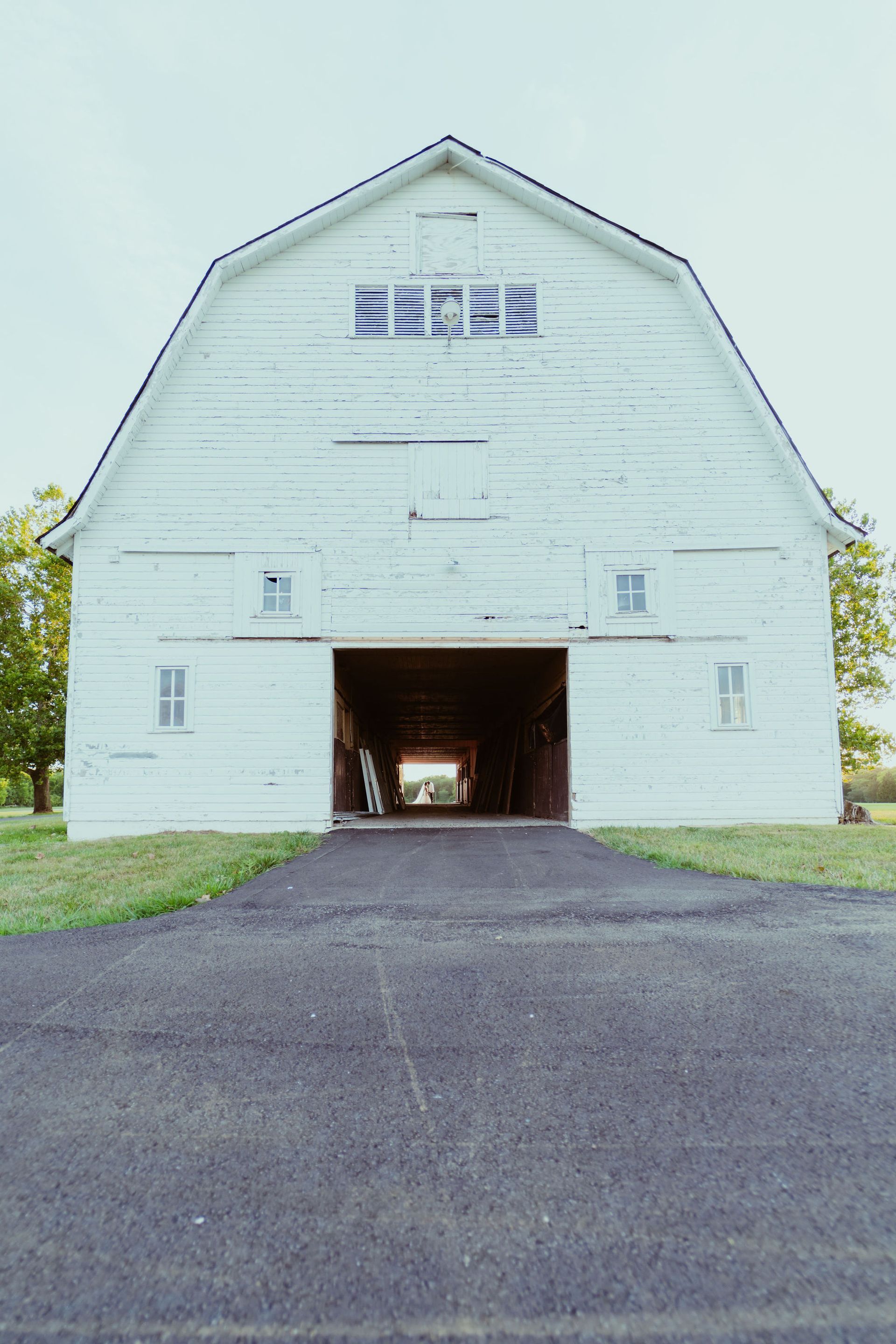 A white barn with the door open and a driveway leading to it.