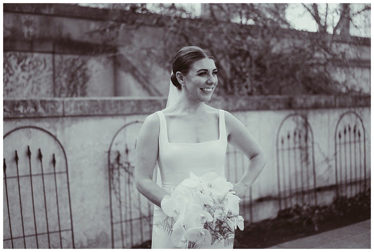 a black and white photo of a bride in a wedding dress holding a bouquet of flowers .