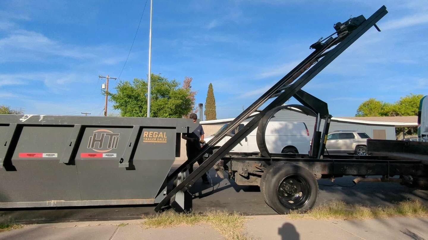 Black dump truck with raised hydraulic bed and extended arm parked outdoors under a blue sky