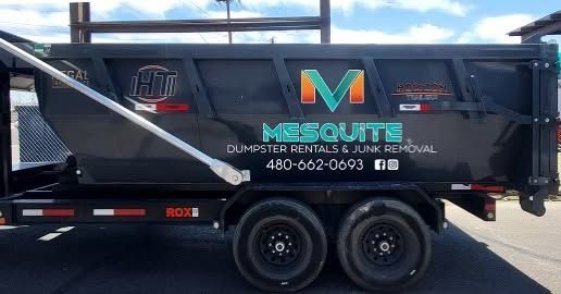 Black dump trailer with Meshute logo and phone number, parked on a sunny street.