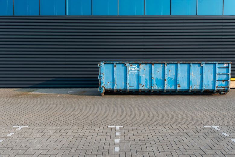 Blue shipping container on a paved lot in front of a dark corrugated wall