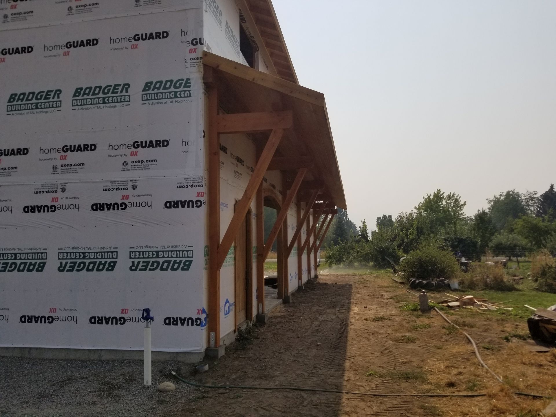 Exterior of a building under construction. Brown wooden beams support a roof overhang. White weather barrier covers walls.