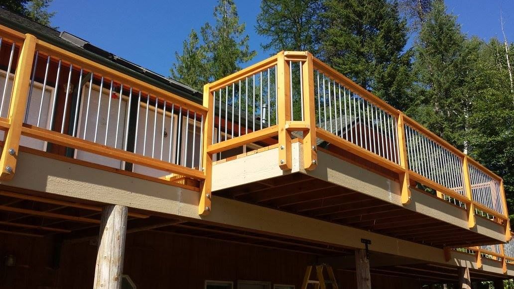 Wooden deck with yellow railing and silver vertical bars, on a sunny day.