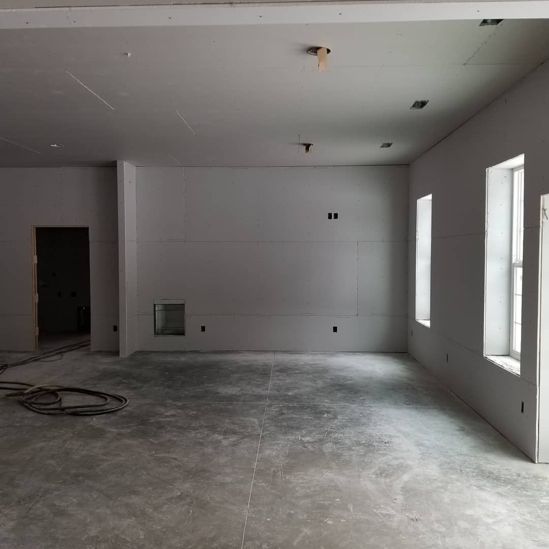 Interior room under construction with gray concrete floor, white walls, and two windows.