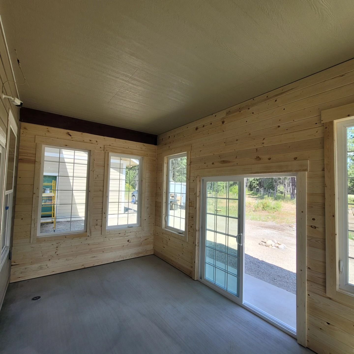 An unfinished room with wooden paneling, windows, and sliding glass door leading to a patio.