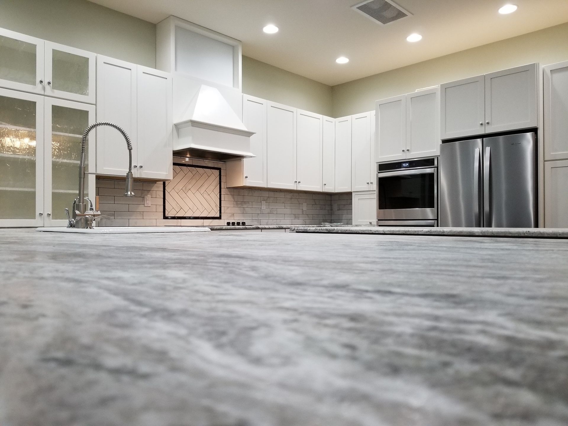 White kitchen with a marble countertop, stainless steel appliances, and a range hood.