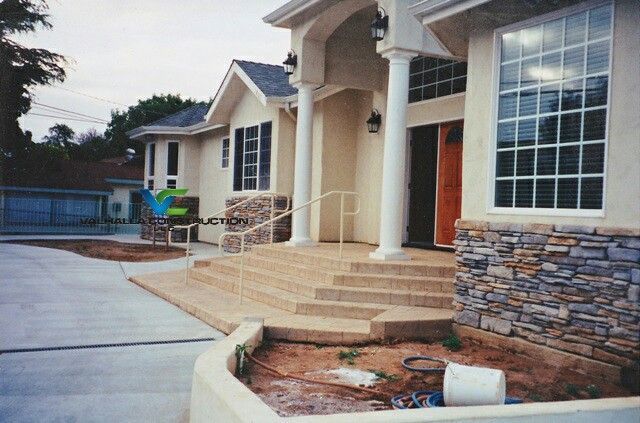 Exterior view of a building with a porch, steps, and columns. The facade is beige with stone accents.
