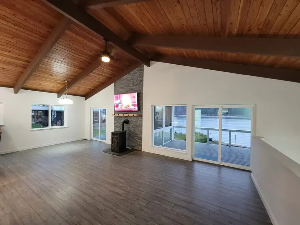 Empty living room with wood ceiling, large windows, and sliding glass doors overlooking water