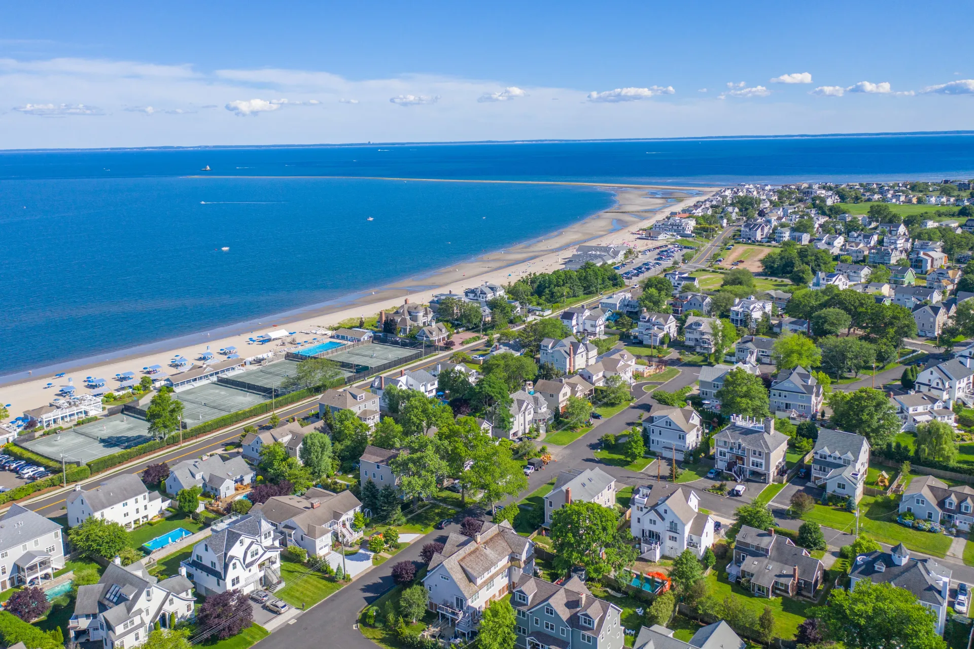 Aerial view of a coastal town with houses, a beach, and blue ocean under a clear sky