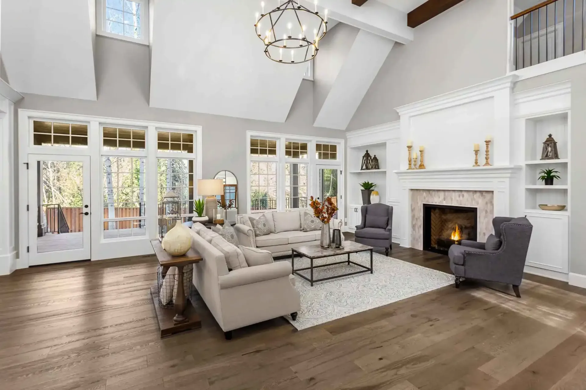 Spacious living room withf ireplace, and large windows; neutral colors, hardwood floors, and a modern chandelier.