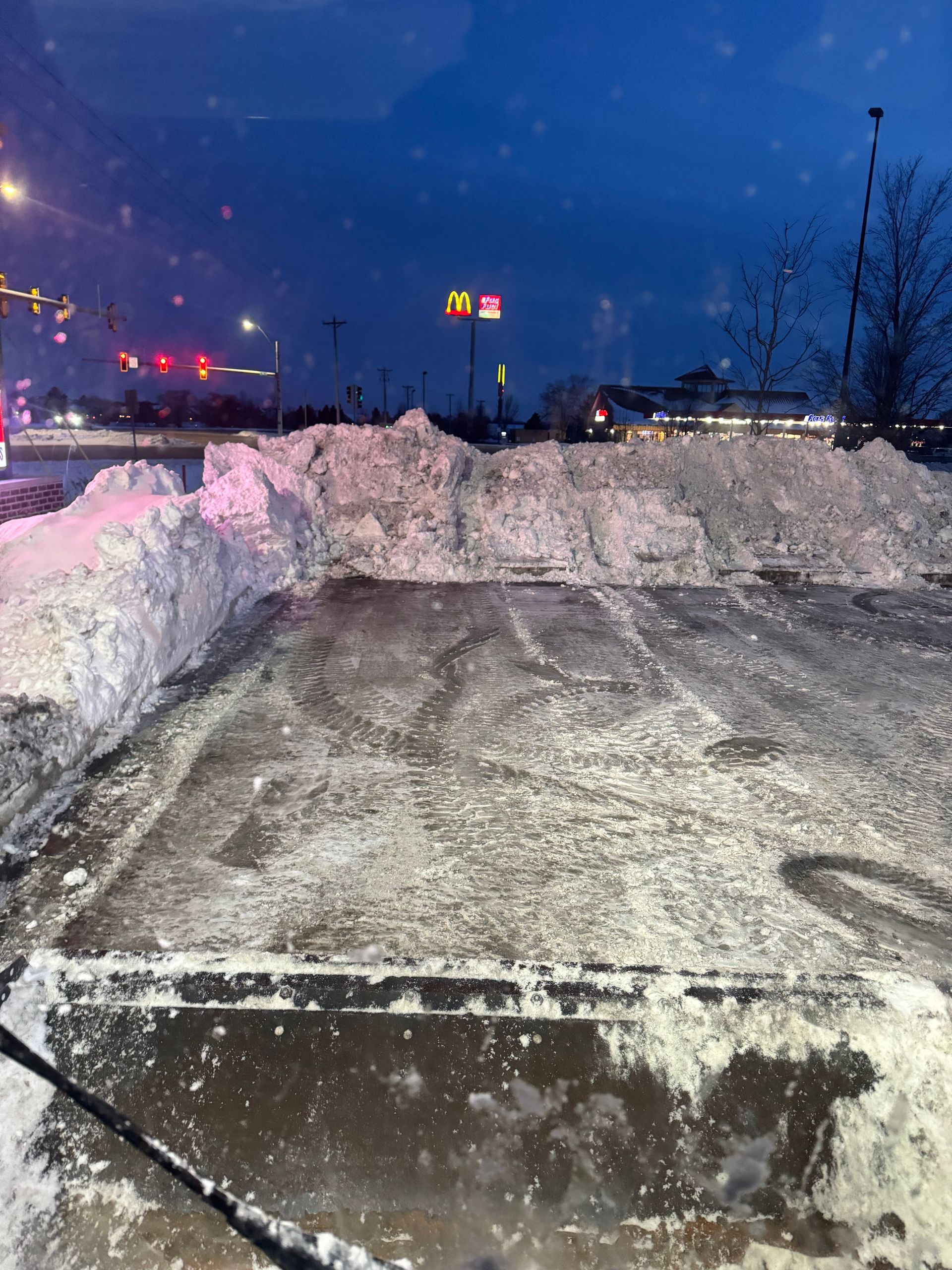 A parking lot covered in snow at night with a mcdonald 's in the background.