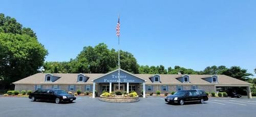 Single-story building with blue roof accents and an American flag, two cars parked in front.