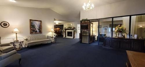 Spacious hotel lobby with blue carpet, cream seating, fireplace, glass doors, and chandelier lighting