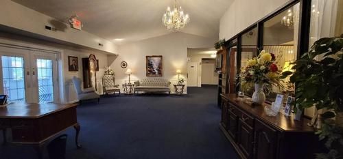 Elegant lobby with blue carpet, chandeliers, white chairs, piano, and flower arrangements