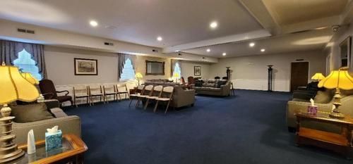Spacious lounge with blue carpet, rows of chairs, sofas, and warm lamps under recessed lighting