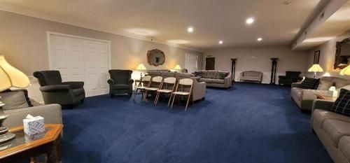 Spacious lounge with blue carpet, sofas, armchairs, and a central table in warm lighting