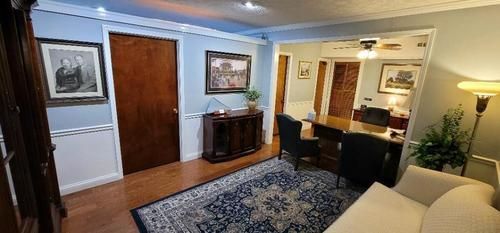 Cozy living room with blue walls, wood floor, patterned rug, desk, lamp, and beige sofa.