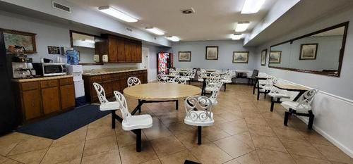Waiting room with white chairs, tables, and framed pictures on beige tile floor