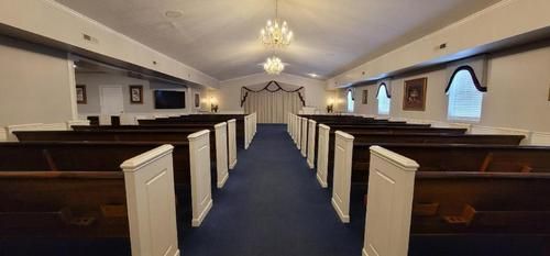 Empty church sanctuary with blue carpet, white pews, and arched windows along the walls
