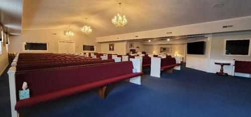 Empty church sanctuary with red pews, white walls, chandeliers, and a blue carpeted aisle